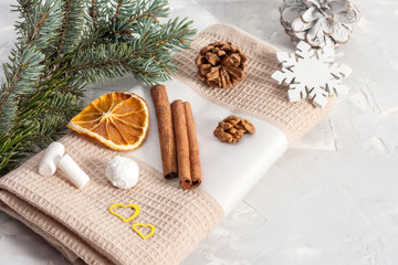 Obraz na płótnie Canvas Cinnamon sticks on a beige napkin with slices of dried orange, pine cone, nuts, snowflakes and marshmallows near a fir branch. Christmas concept. Copy space.