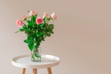 Fototapeta premium Bouquet of pale pink roses in a glass vase on white table on neutral background wall