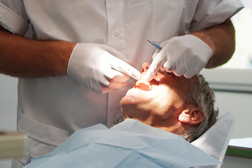 Caucasian Man at the dentist, having his teeth checked. Hands with gloves holding a mirror in hand,...
