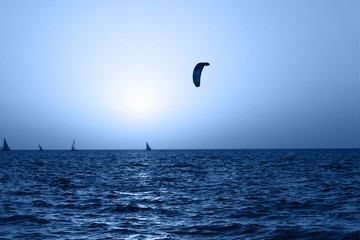 Kite-surfing and yachts on orange sunset background