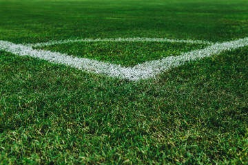 White corner line on green grass at football or soccer stadium.