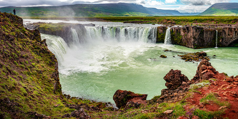 Panoramic view over powerful and wide waterfall Godafoss with a lonely traveler standing at its high cliff, Iceland, summer, scenic view
