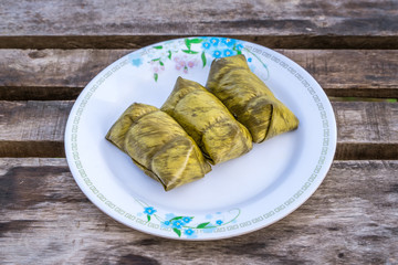 Thai Desserts, Sticky rice wrapped in banana leaves, Porridge tie on white disk and wooden table.