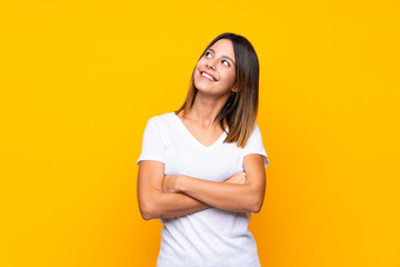 Young woman over isolated yellow background looking up while smiling