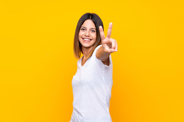 Young woman over isolated yellow background smiling and showing victory sign