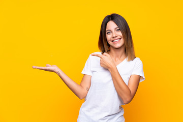 Young woman over isolated yellow background holding copyspace imaginary on the palm to insert an ad