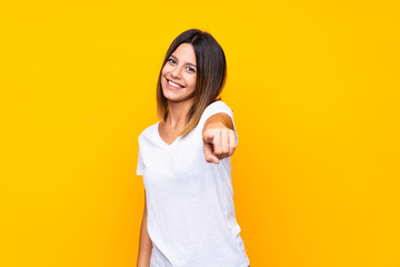 Young woman over isolated yellow background points finger at you with a confident expression