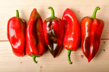 Five fresh organic red peppers on a raw wooden table ready to be cooked, top view or flat lay of healthy vegan food