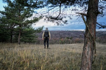 Man walking in between trees on dry grass with backpack on. Hiker hiking between trees with backpack on