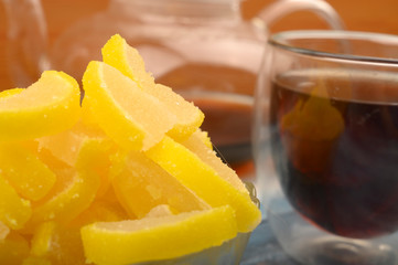 Marmalade lemon slices, a glass of black tea and a teapot with brewed tea on a wooden background. Sweet dessert. Close up.