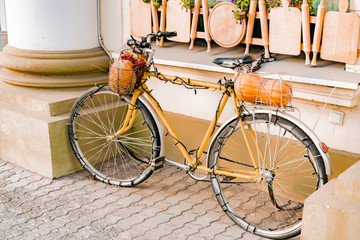 Fototapeta na wymiar Old bicycle with pumpkin and Christmas-tree lights on it stands near the building as a decoration. Design. Halloween. Vintage. Style. Exterior
