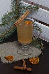 Orange drink in a glass goblet. A slice of dried orange floats in it. Nearby are cinnamon sticks and dried oranges.
