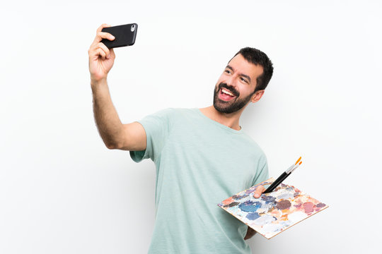 Young artist man holding a palette over isolated background making a selfie