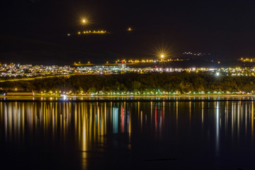 Obraz premium Akureyri at night, in the foreground mirroring water with the lights of the city reflecting in the water,