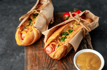 french hot dogs from the store  packed in paper, baked with cheese and mustard on a stone background 