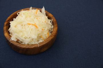 Tasty sauerkraut or fermented cabbage in a wooden bowl isolated on a blue background. Fermented food. Ingredient for bigos. With copy space for text.