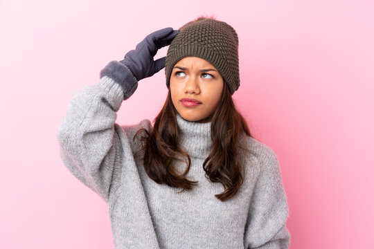 Young Colombian girl with winter hat over isolated pink wall having doubts and with confuse face expression