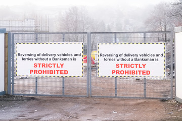 Banksman required for reversing of vehicles sign at gate entrance on building construction site and strictly prohibited text