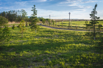 Obraz premium Winding alley with lanterns near the green grass for walk goes into the distance to the large mountains against the blue sky.