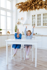 two children sitting on the kitchen table and eating candies. Mother with daughter and toddler son having breakfast at home. Happy lifestyle family moments.