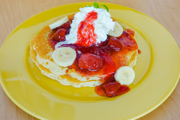 Pancakes served with banana, strawberry, strawberry jam and whipped cream
