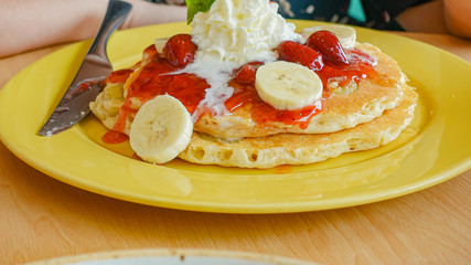 Pancakes served with banana, strawberry, strawberry jam and whipped cream