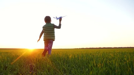 A happy little boy runs across a green meadow, launching a plane into the sky.