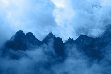Blue toned rocky mountain ridge in foggy clouds