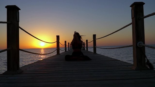 Woman practicing Yoga during beautiful Sunrise at the seaside.