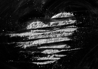 White powder in shape heart, cocaine line isolated on black background, top view, series