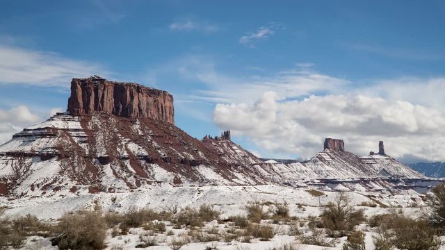Timelapse viewing desert buttes and towers in Castle Valley during winter as snow covers they landscapes and clouds move through the sky.