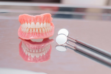 Fototapeta na wymiar Two dentures. Instruments and dental hygienist checkup concept with teeth model dentures and mouth mirror. Regular dentist checkups