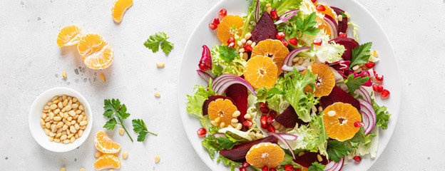 Christmas salad with boiled beet, red onion, tangerines, pomegranate, parsley, pine nuts and lettuce leaves, banner