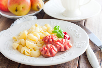 Fried sausages with pasta on a wooden plate on a wooden table, selective focus