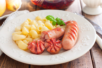 Fried sausages with pasta on a wooden plate on a wooden table, selective focus