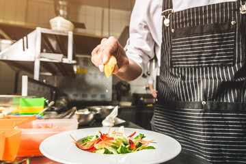 Professional chef cooking in the kitchen restaurant at the hotel, preparing dinner. A cook in an apron makes a salad of vegetables and pizza.