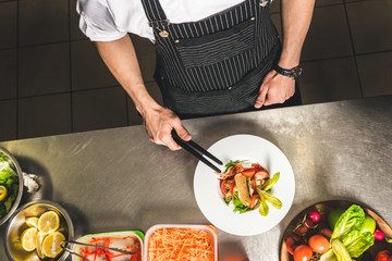 Professional chef cooking in the kitchen restaurant at the hotel, preparing dinner. A cook in an apron makes a salad of vegetables and pizza.