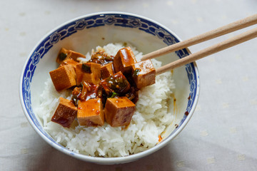 Bowl with tofu, rice and soya sauce. Served with wooden chopsticks.