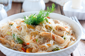Funchosa with vegetables and chicken on a white plate on a wooden table, selective focus