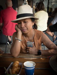 Asian woman in white hat sitting at cafe table with dish of lukamades