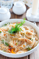 Funchosa with vegetables and chicken on a white plate on a wooden table, selective focus