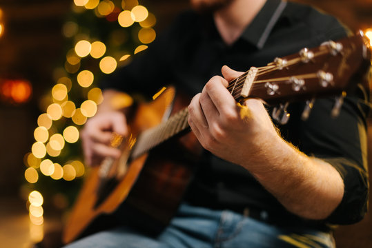 Male plays guitar close-up. Against the background of a decorated Christmas tree with a bokeh effect.