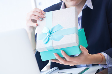 Christmas, any holiday. Office employee received a gift from her colleagues. Closeup woman hands holds gift box on office background.
