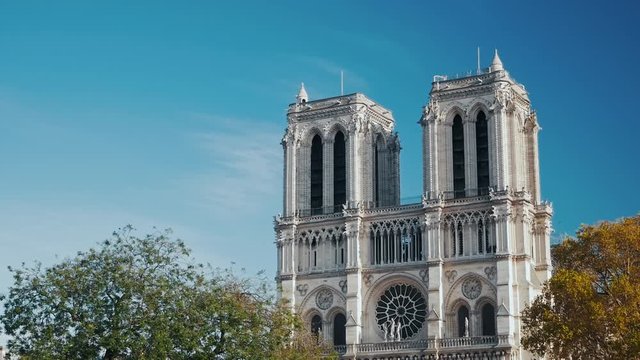 The facade of Notre Dame Cathedral emering above orange colored trees in a beautiful Autumn day