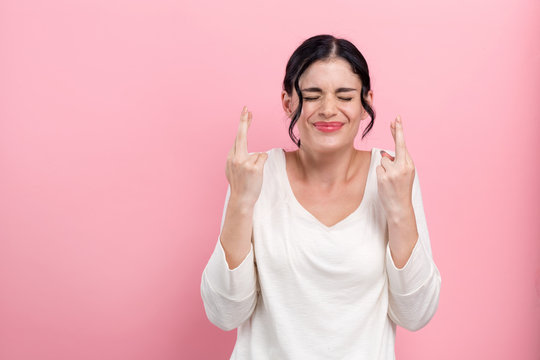 Young woman crossing her fingers and wishing for good luck on a pink background
