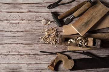 Working tool of a carpenter. Old wooden jointer, hammer, chisel, saw-hacksaw with small teeth, pliers, folding meter, boards and shavings on a wooden background.