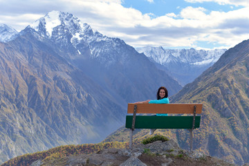 A young woman sits on a bench at the top of a mountain in autumn