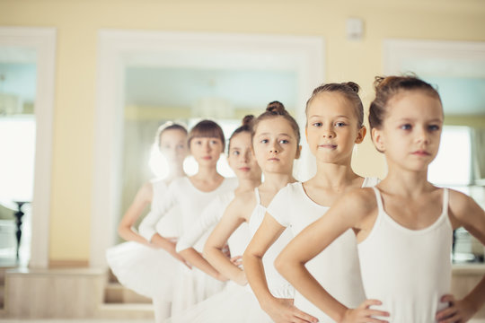 group of caucasian cute girls 7-8 years old dancing classic ballet together wearing white tutu skirts and pointe shoes
