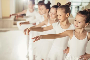 Fotobehang Dansschool little kids ballerinas in studio, wearing white tutu skirts, stand in pose, performing classic ballet dance, smooth movements