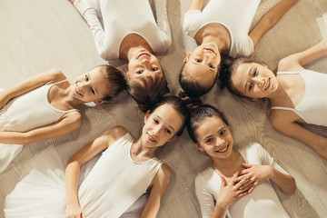 awesome attractive ballerinas beginners lying on floor in circle and looking at camera, happy caucasian ballerinas in tutu skirts